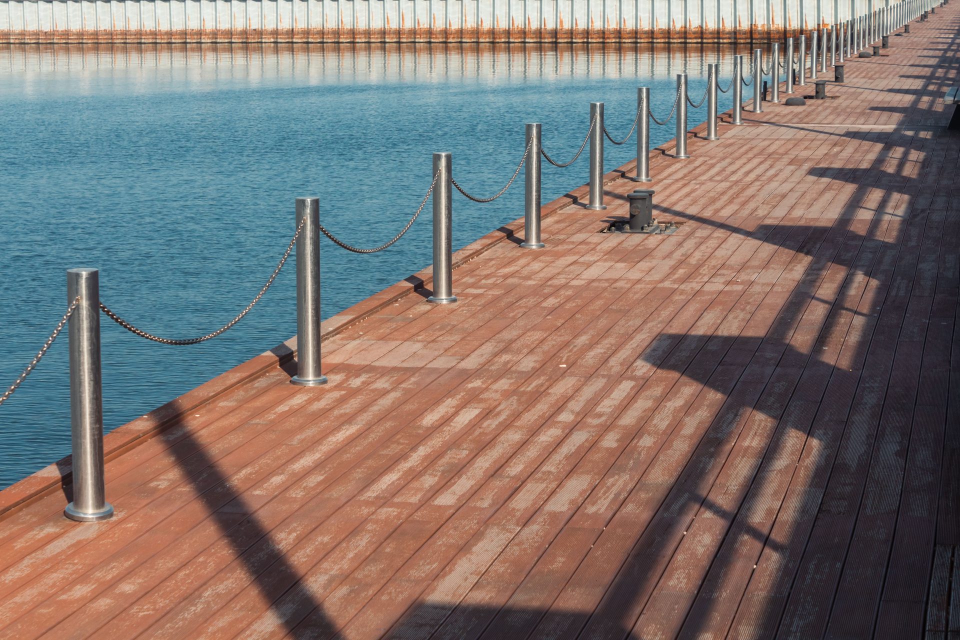 A sunny view of a wooden pier with shadows cast over blue water, ideal for coastal themes.